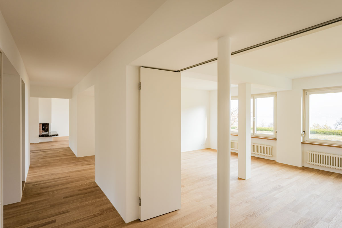 gang-blick-vom-entree-richtung-wohnzimmer-mit-cheminee-und-raum-nischen-bei-den-zimmern-und-offener-faltwand