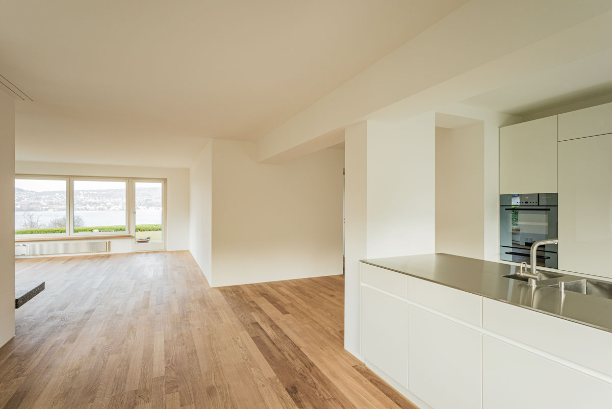 helles-wohn-ess-zimmer-mit-seeblick-parkett-schiffboden-eiche-geoelt-moderner-offener-weisser-kueche-und-edelstahl-abdeckung