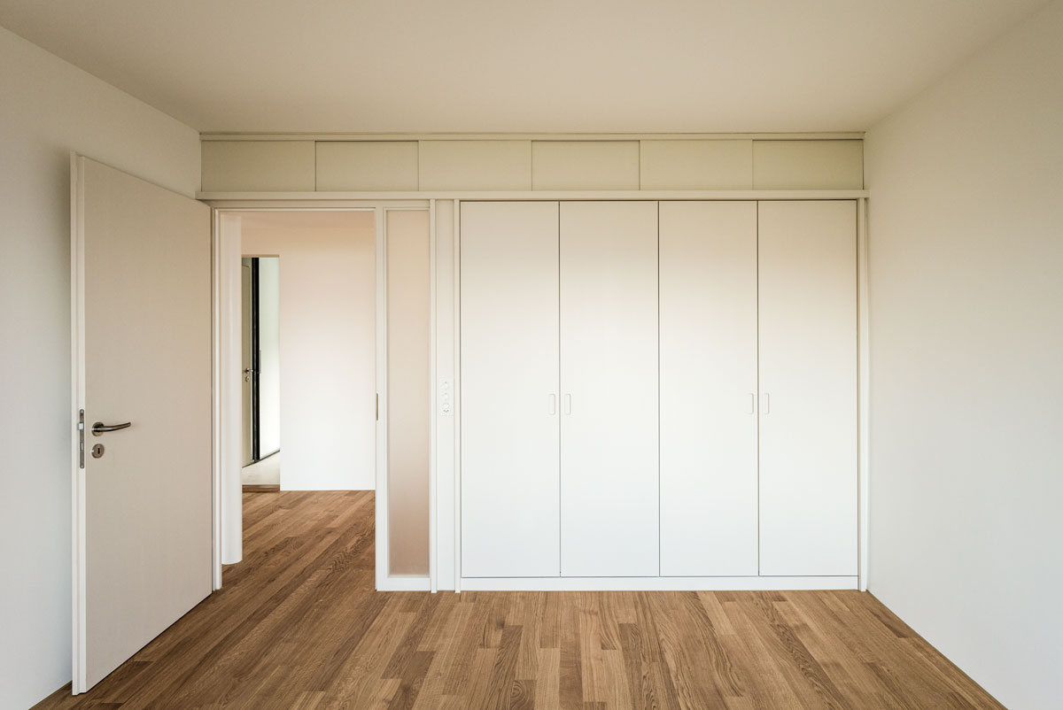 zimmer-mit-eichenparkett-schiffboden-tuer-mit-mattglas-element-und-minimalistischen-modernen-einbauschraenken