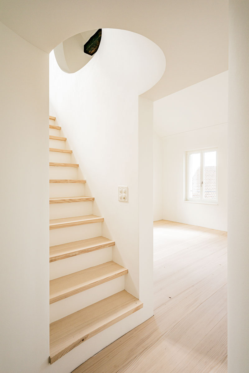 durchgang-zum-hellen-hohen-raum-mit-holzboden-tanne-geseift-und-treppe-zur-galerie-mit-runder-oeffnung-und-gewoelbe