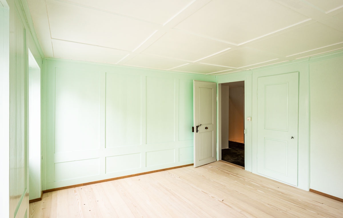 restauriertes-zimmer-mit-hellem-gruenem-wand-taefer-hellgrauer-tuere-sowie-holzboden-tanne-geseift-mit-blick-zum-vorraum