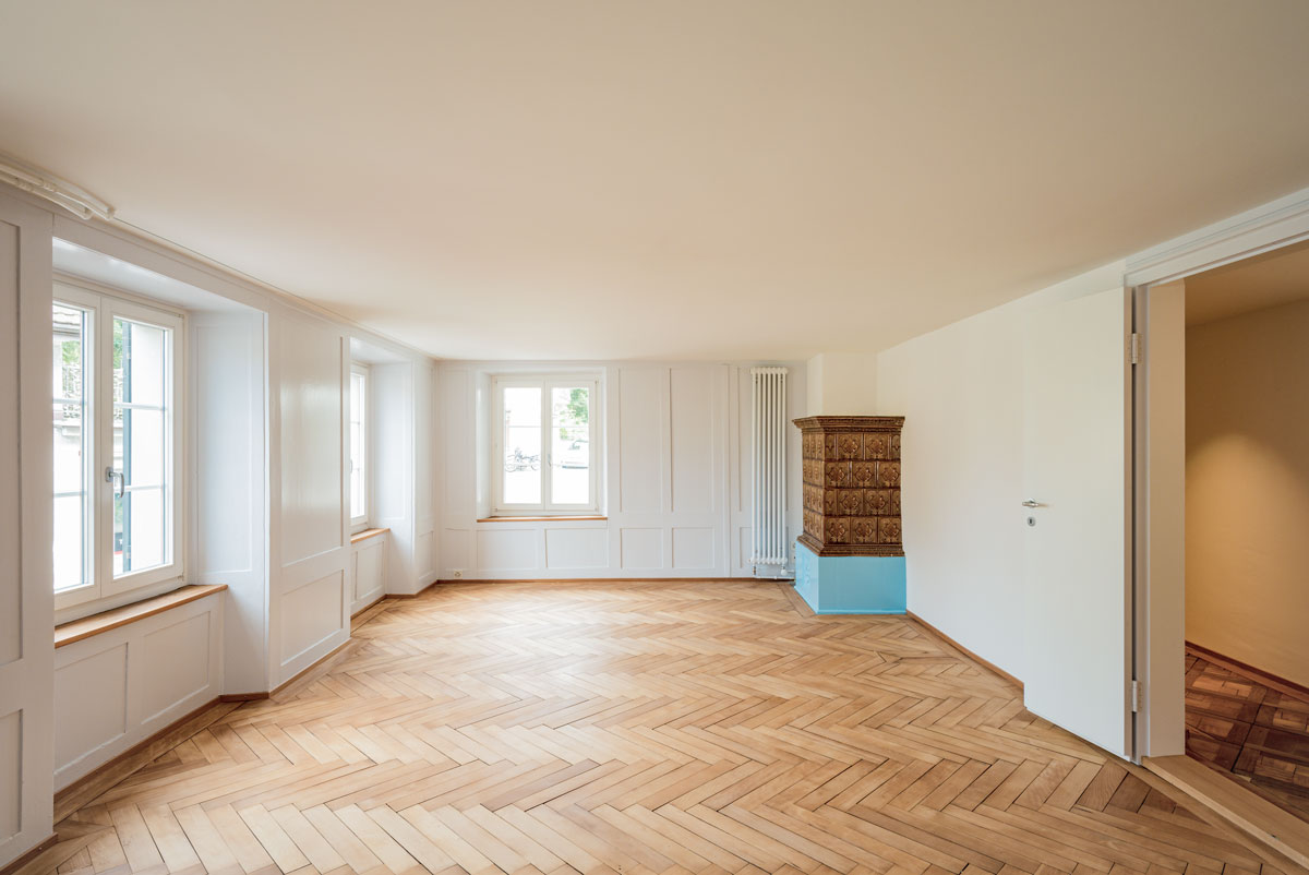 wohnzimmer-mit-historischem-hellblauem-taefer-braun-blauem-kachelofen-und-fischgrat-parkett-in-eiche