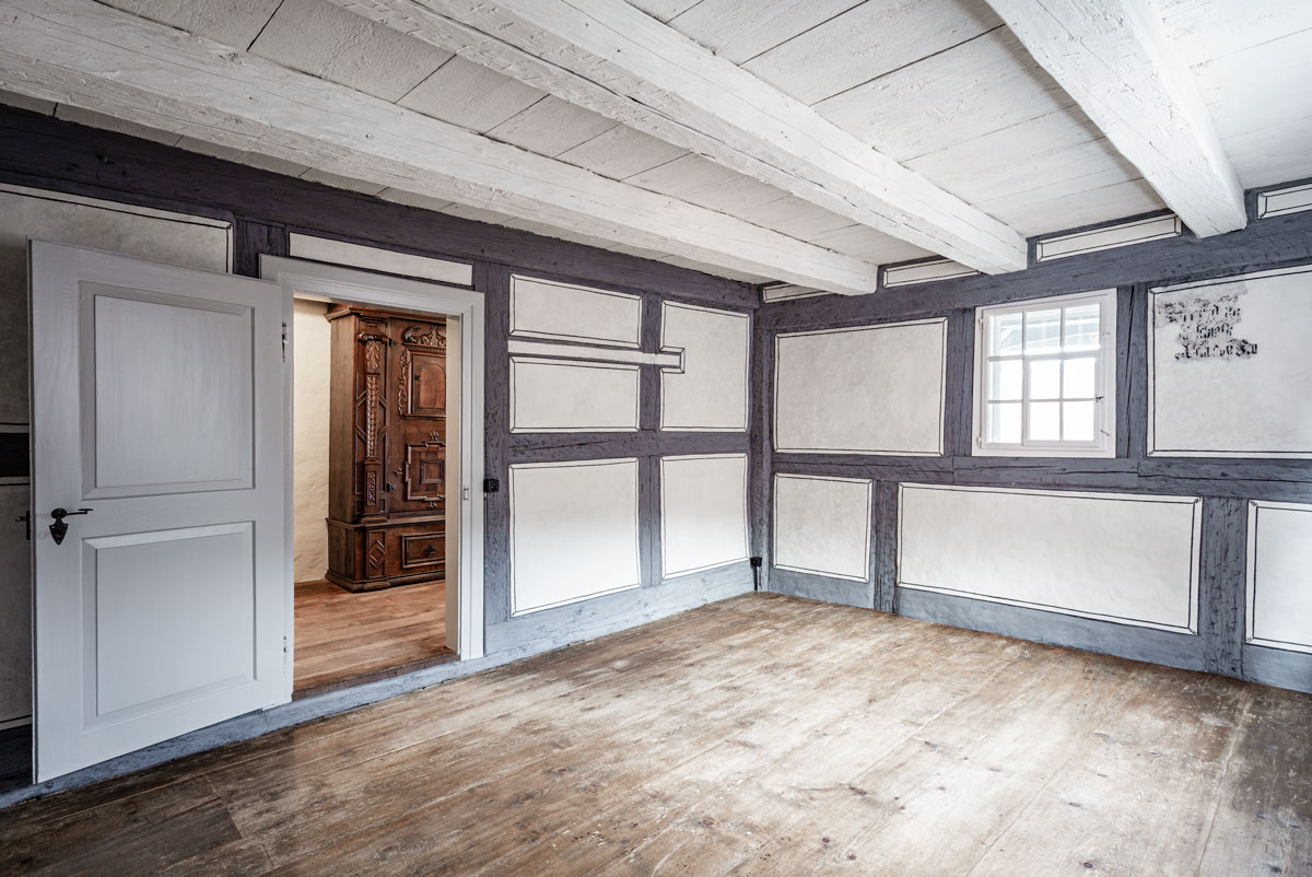 historisches-zimmer-mit-restaurierten-riegelwaenden-in-grau-mit-weissen-fuellungen-und-begleimalerei-aus-der-zeit-um-1600