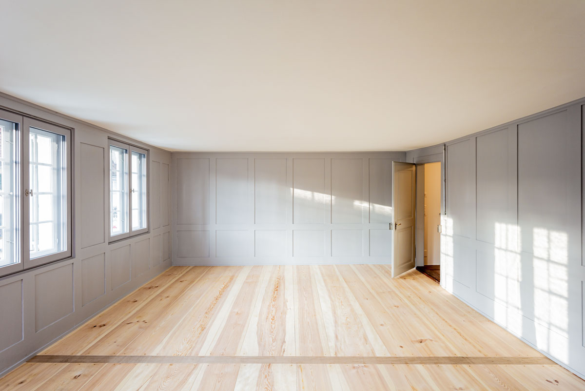 helles-zimmer-mit-hellgrauem-wandtaefer-weisser-gipsdecke-und-neuem-holzriemenboden-mit-kernholz