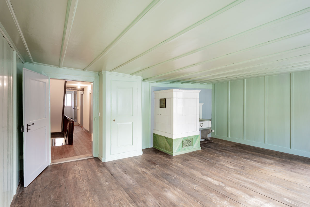restauriertes-historisches-zimmer-mit-kachelofen-und-gruenem-taefer-barock-sowie-holzboden-mit-patina