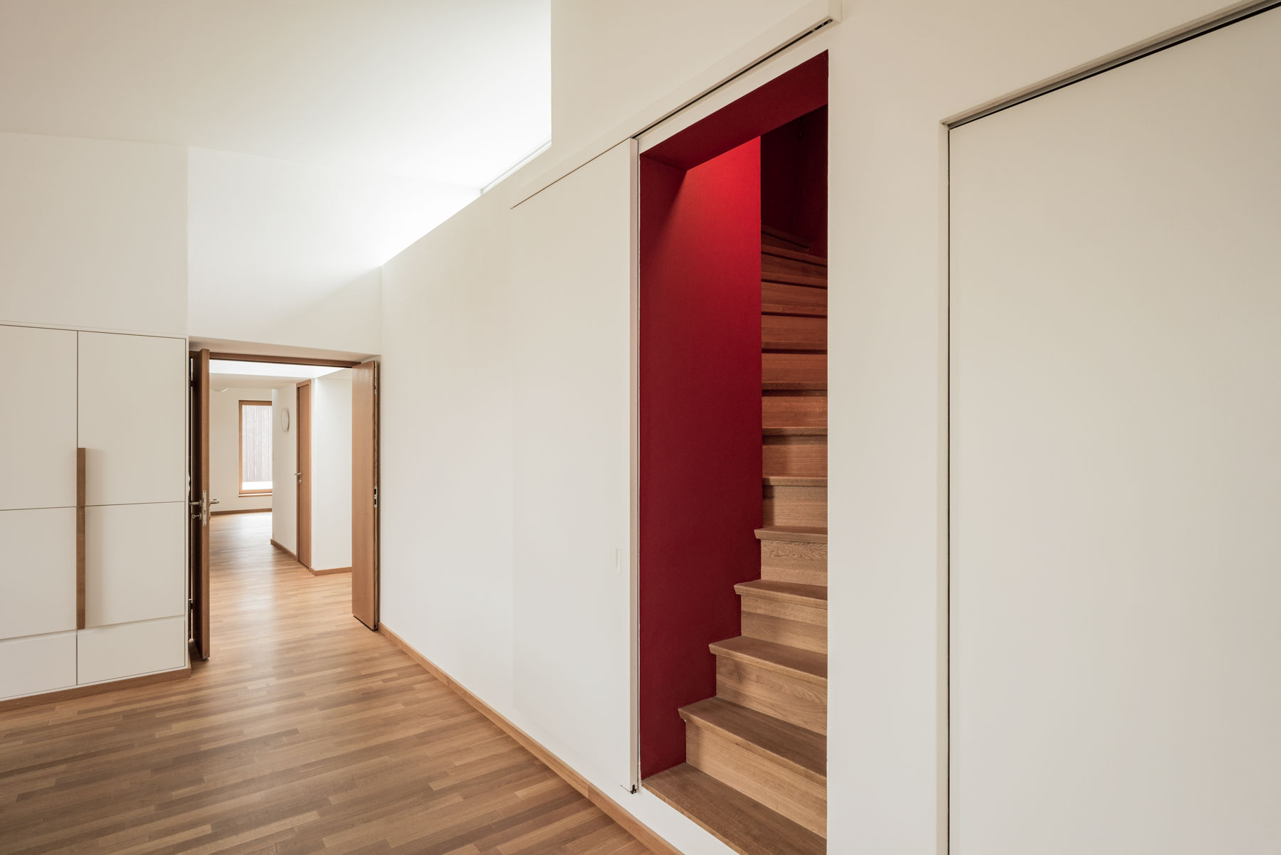 sitzungs-zimmer-mit-hinter-einer-schiebetuer-versteckten-steilen-treppe-zur-terrasse-mit-roten-waenden-und-oberlicht