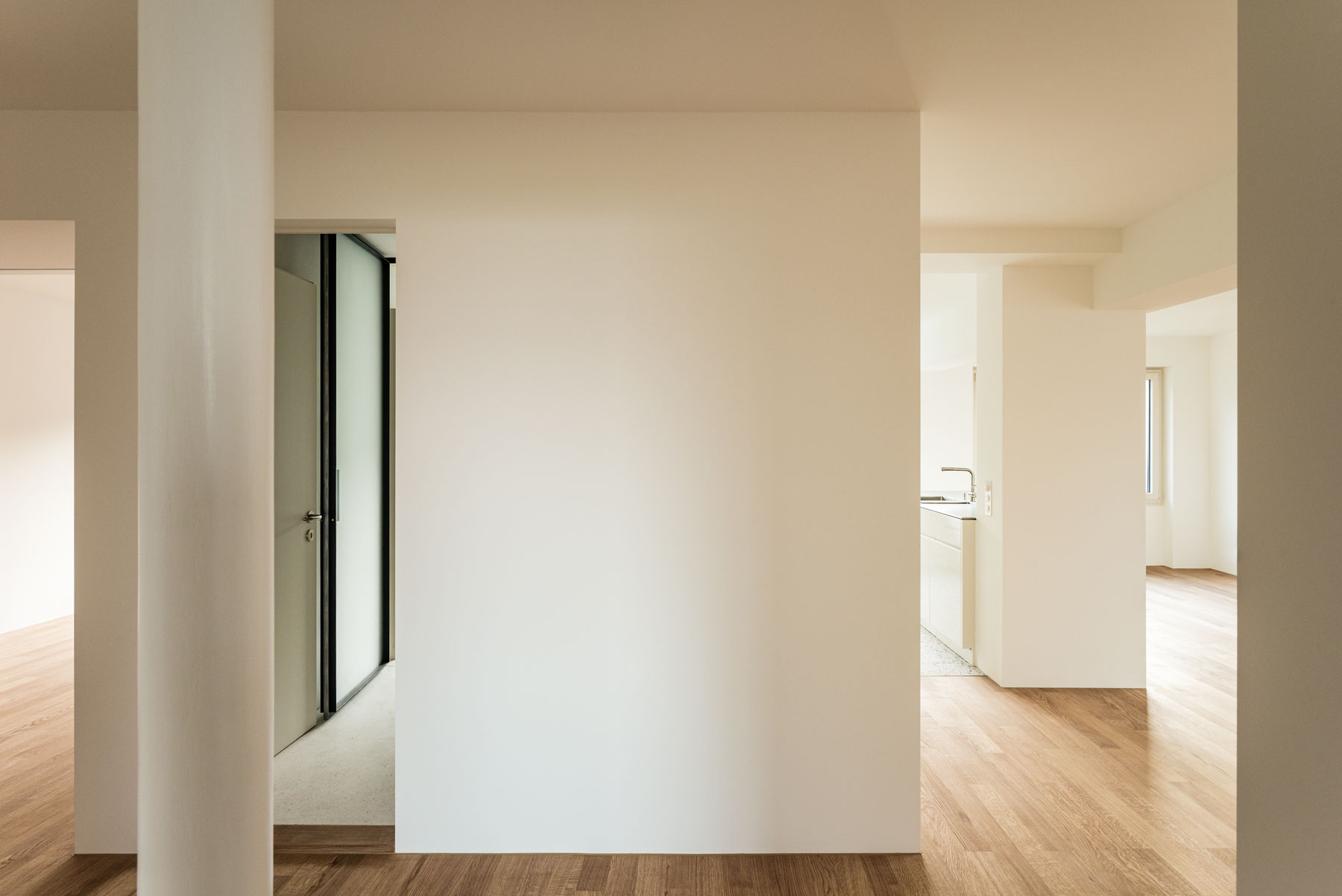 gang-mit-runder-stahlstuetze-und-blick-zum-esszimmer-mit-offener-kueche-und-bad-dusche-mit-terrazzo-boden